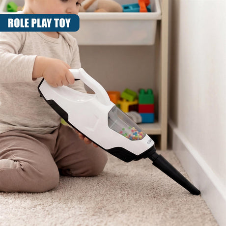 Child operating a white and black toy vacuum cleaner, containing colorful beads, near a baseboard.