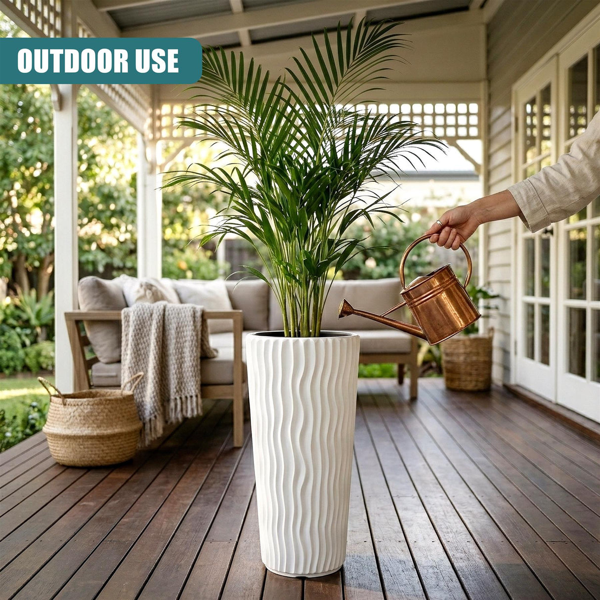 Tall white planter pot with vertical fluting holds a potted green plant on a wooden deck.