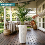 Tall white planter pot with vertical fluting holds a potted green plant on a wooden deck.