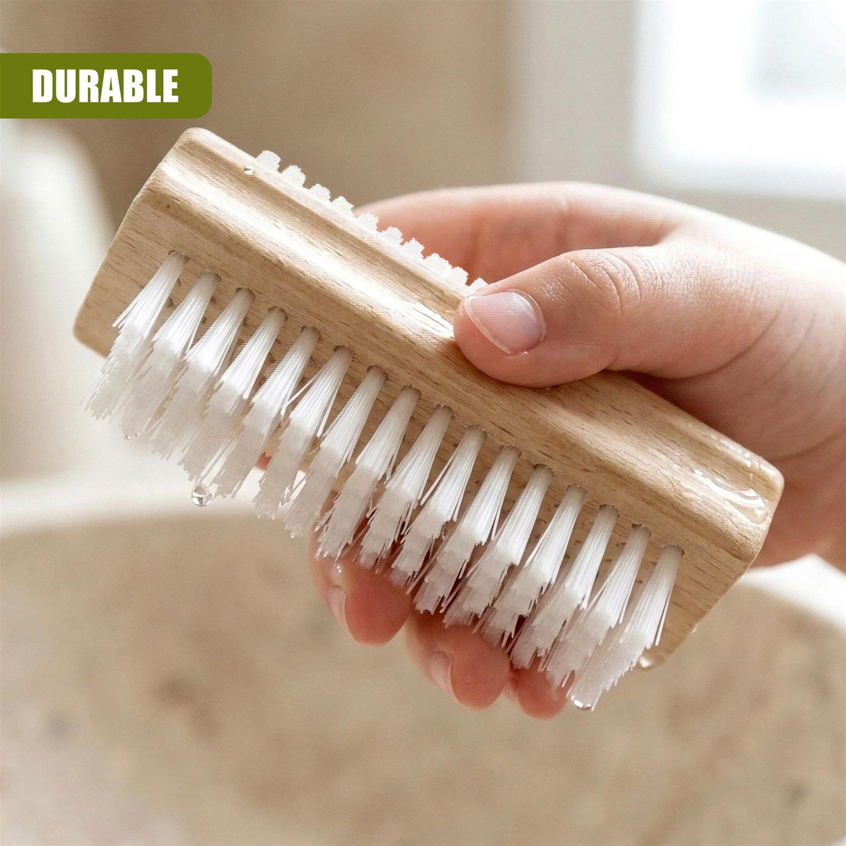 A hand holds a wooden nail scrubbing brush featuring stiff white bristles for cleaning.