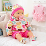 The doll is dressed in a striped pink hat, patterned sweater, and pink shorts.