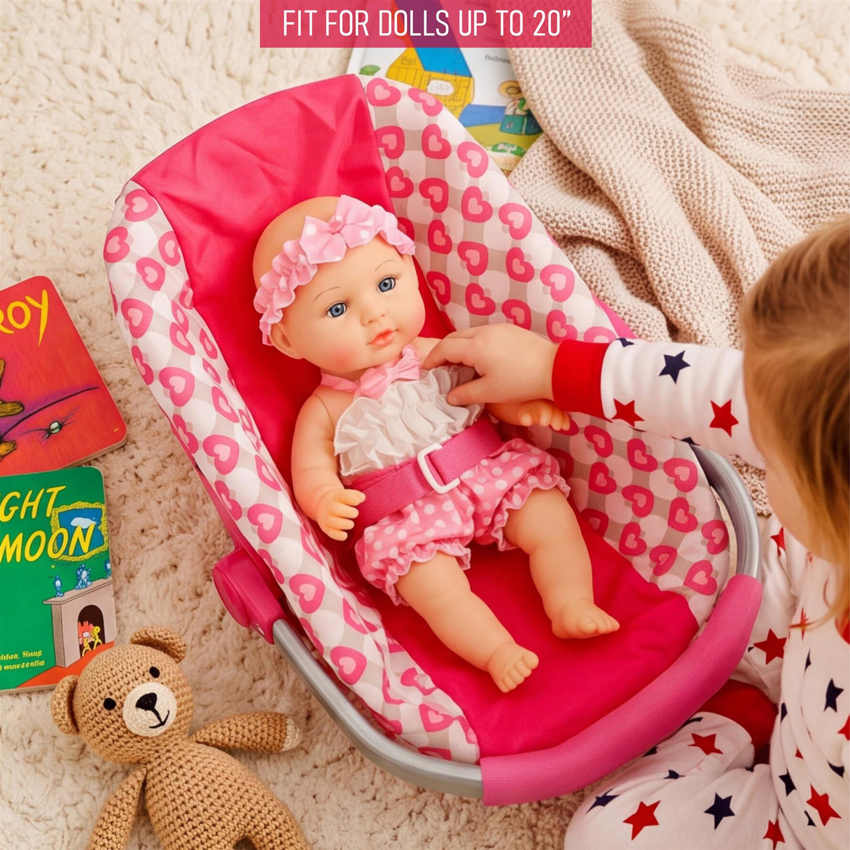 A small doll sits in a pink and white padded car seat, being held by a child's hands.