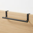 Black horizontal rail supported by brackets, mounted to a light wood paneling surface.