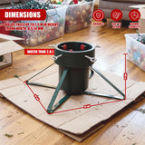 A green metal Christmas tree stand on a wooden floor, surrounded by storage boxes and cardboard packaging