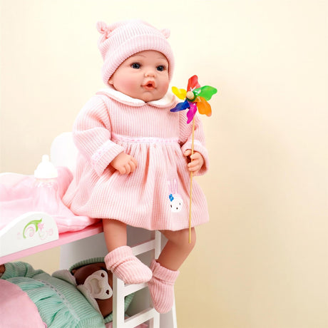 Doll dressed in a pink knit outfit, hat, and socks, holding a colorful flower.