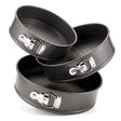 Three sized black springform baking tins are stacked on a white background.