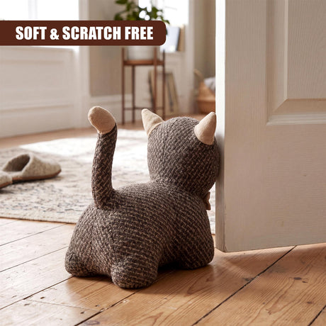 A crocheted gray kitten figurine stands as a door stopper next to a white painted door.