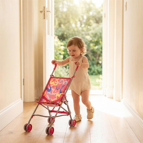 Little girl pushes a pink and red floral patterned doll's buggy in a sunny room.
