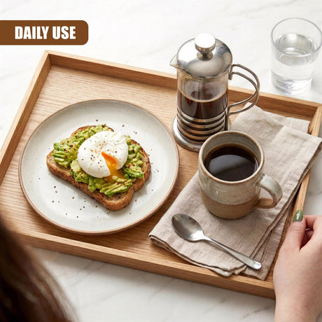 On a wooden tray are avocado toast, a cafetiere, a mug of coffee, and a glass of water.