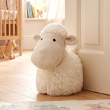 White, fluffy sheep noveliy door stopper standing against a light wooden door.