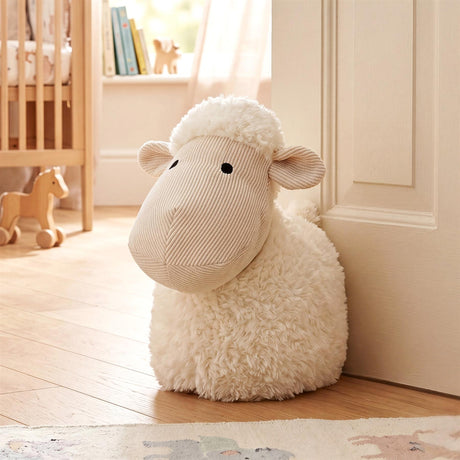 White, fluffy sheep noveliy door stopper standing against a light wooden door.