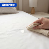 A hand uses a folded cloth to pick up a visible droplet of liquid on the white bed sheet.