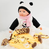 Bebi doll with scarf in panda outfit, sitting on a blanket with giraffe and zebra patterns.