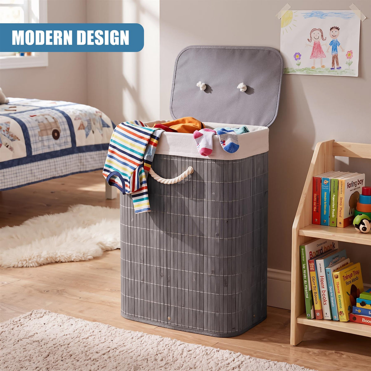 A grey bamboo laundry hamper with a lid and rope handle, filled with clothes, sits on a wooden floor next to a bookshelf in