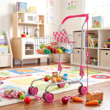 Metal kids shopping trolley filled with toy groceries, standing on a patterned play rug with colored props.