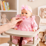 Hand holds pink pacifier near a doll dressed in pink, seated in a baby rocking chair.