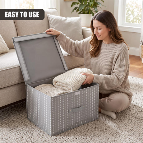 A woman sits on a rug placing folded blankets into a grey heart-patterned storage box with an open lid, next to a sofa