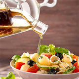 A glass oil and vinegar dispenser pouring liquid over a fresh pasta salad filled with tomatoes, olives, cucumber, and basil. The background features warm wooden tones, enhancing the appetizing appearance of the dish. Perfect for kitchen use and entertaining. Available at ukbuyzone.