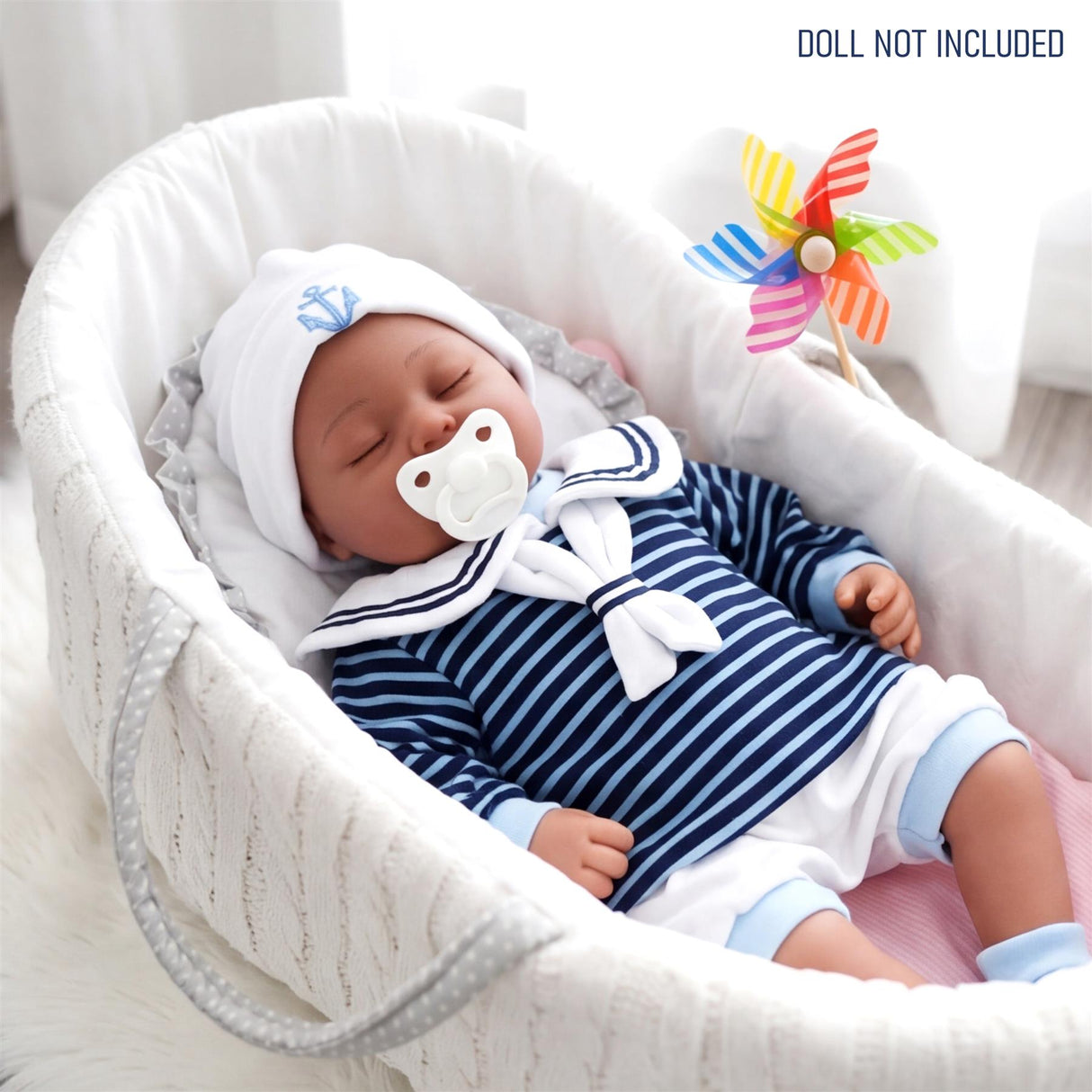 A reborn doll dressed in a striped blue and white sailor outfit lying in a white baby bassinet.