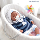 A reborn doll dressed in a striped blue and white sailor outfit lying in a white baby bassinet.