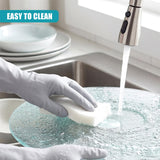 A glass cake stand is being washed with a sponge under running faucet water in a sink.