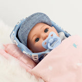 A small doll wrapped in a blue blanket, wearing a hat with a white design, is lying in a pink stroller.