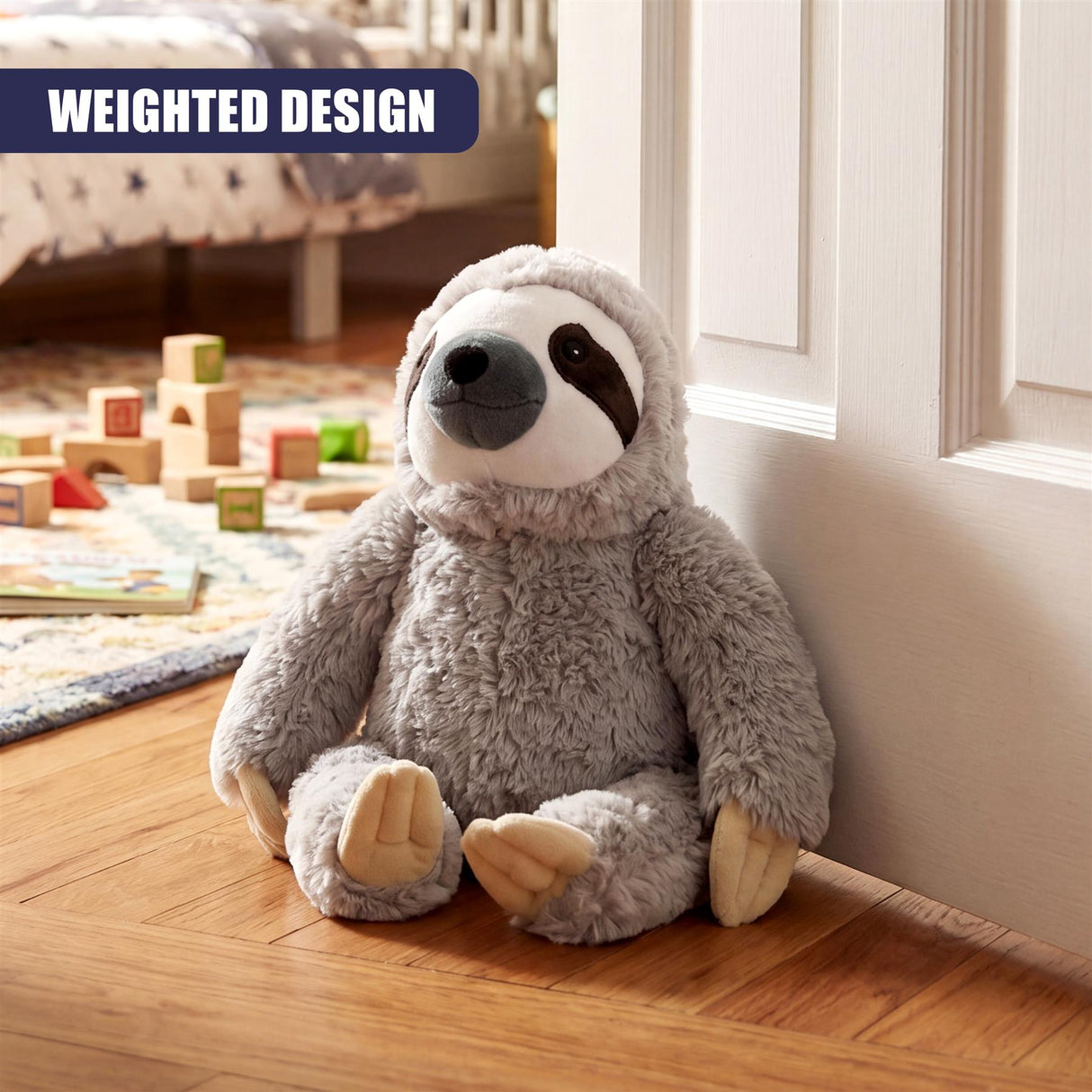 A gray stuffed sloth door stopper rests on a wooden floor next to a white baseboard.