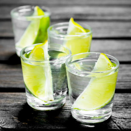 Three shot glasses with sliced lime on the rims, on a wooden table.