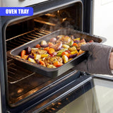 Roasting tin containing roasted root vegetables and pieces of protein inside a dark oven.