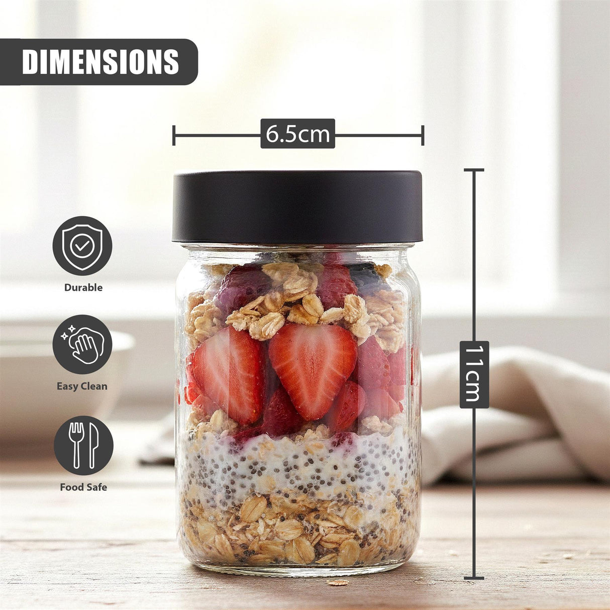 A glass jar with a black lid is filled with a visible mixture of granola, sliced strawberries, and oats.