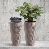 Two tall, ribbed brown planters are shown, one holding a variegated green houseplant.
