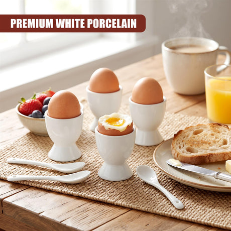 Set of four white ceramic egg cups with spoons on a wooden table with toast, fruit and coffee