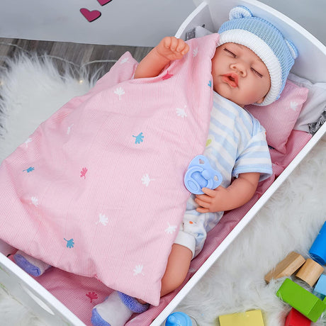 This image shows a baby doll lying in a pink baby bassinet with an attached blanket, wearing a blue and white knit cap, dressed in a onesie, surrounded by toys. The doll has a pacifier in its mouth, and there are colorful blocks in the corner of the photo. - UKBuyZone