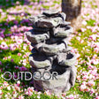 Multi-tiered stack of artificial gray rocks resting on vibrant green lawn and scattered pink blossoms.