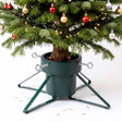 A green metal Christmas tree stand holding a decorated tree against a white background