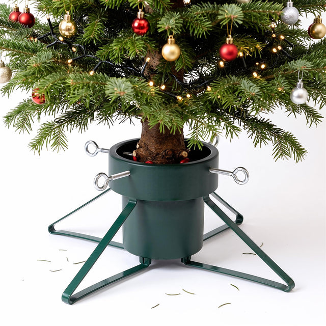 A green metal Christmas tree stand holding a decorated tree against a white background