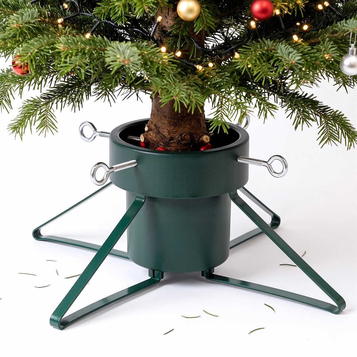 A green metal Christmas tree stand holding a decorated tree, featuring four adjustable bolts and a water reservoir base
