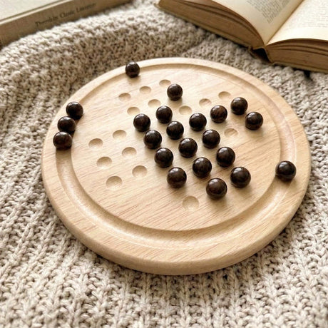 Wooden solitaire board game with multiple indentations and dark wooden playing tokens scattered on it.