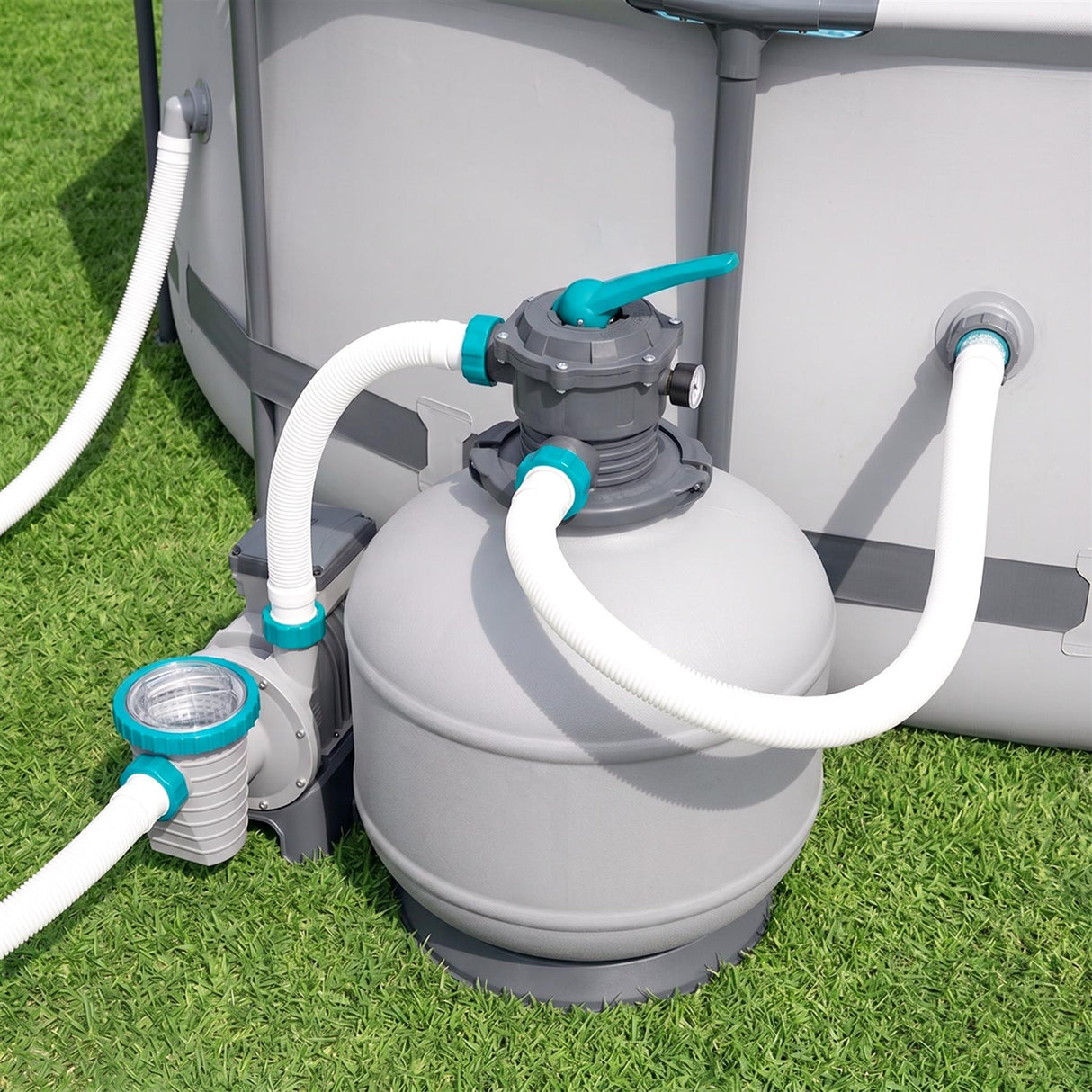 Gray water filter unit with connected pipes stands on grass next to a large rectangular housing.