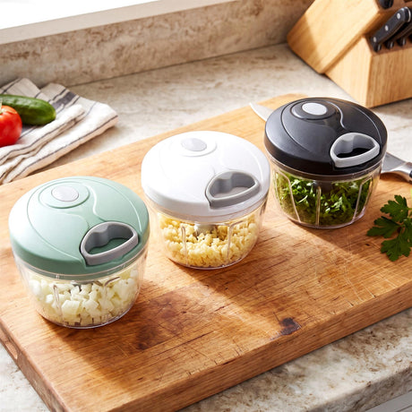 Three manual food choppers filled with chopped ingredients are arranged on a wooden cutting board.