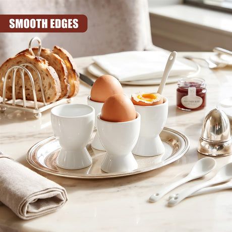 A set of four white ceramic egg cups with spoons on a silver tray, accompanied by bread and jam on a marble table