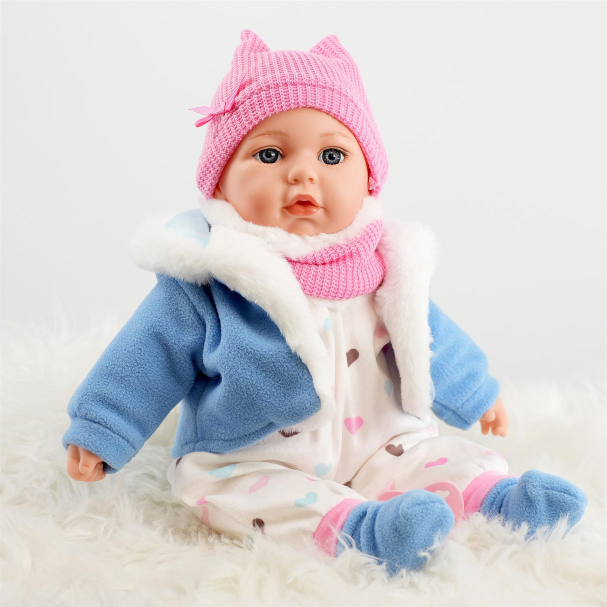 A baby doll wearing a blue jacket with a hood, pink hat and purple blanket.