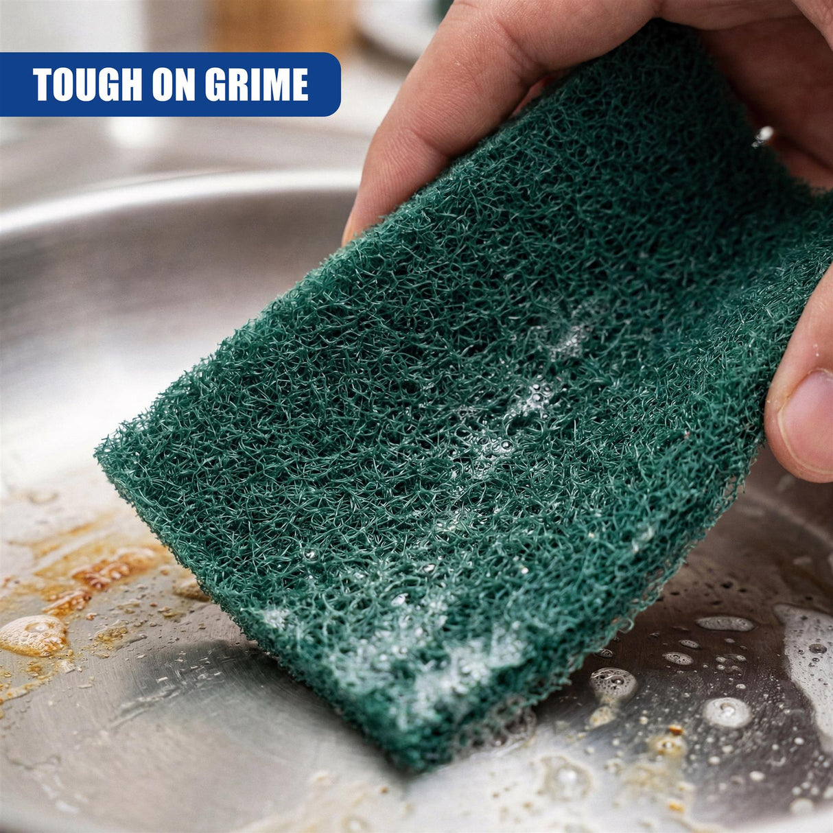 A hand holds a dark green scouring pad over a dirty, wet stainless steel sink surface.