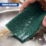 A hand holds a dark green scouring pad over a dirty, wet stainless steel sink surface.