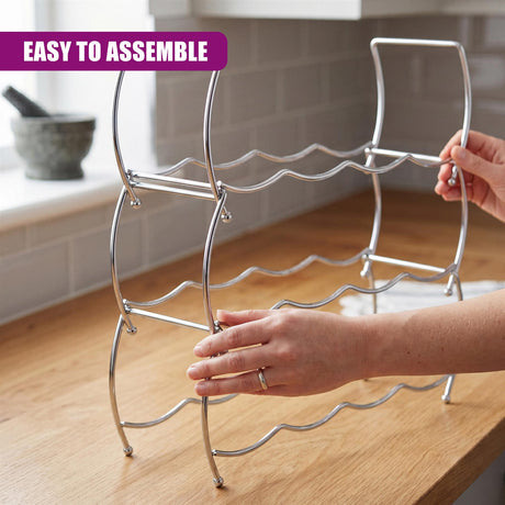 Silver metal wine rack with curved supports is held on a wooden surface by human hands.
