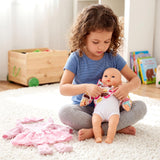 Young girl holding a baby doll while surrounded by pink accessories on a cream rug.