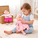 A child in blue overalls holds a pink-dressed doll while sitting near a woven basket of clothes.