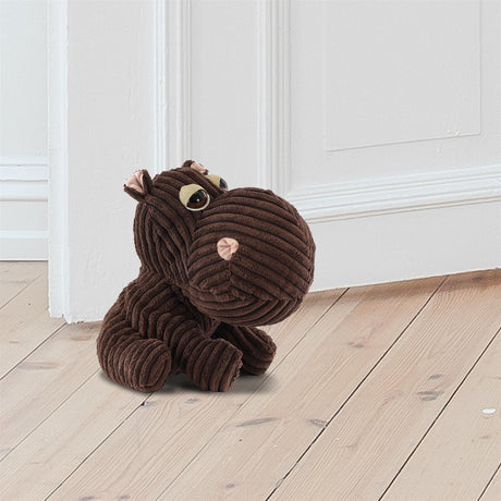 A brown corduroy hippo doorstopper sits on a wooden floor against a white wall