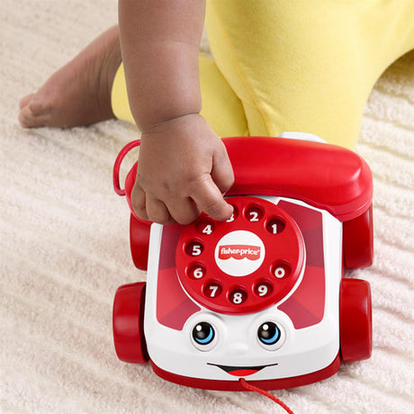 The red toy telephone features a dial and face, with a small hand reaching toward the numbered buttons.