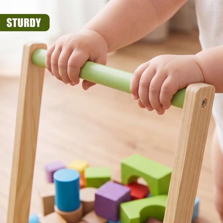Wooden baby walker with a green bar is shown, surrounded by multi-colored wooden blocks on the floor.